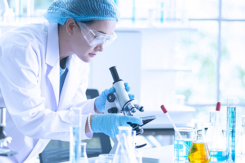 woman in lab coat looking into microscope